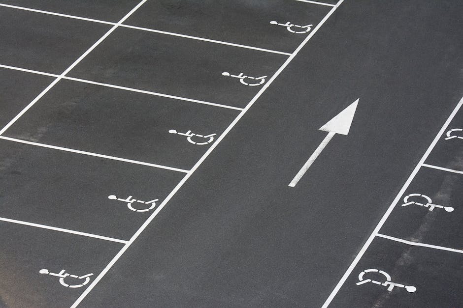 A section of an outdoor parking lot showing clearly marked designated parking spaces with white lines and symbols for disabled access, all on a dark asphalt surface. In the center of the image, there 